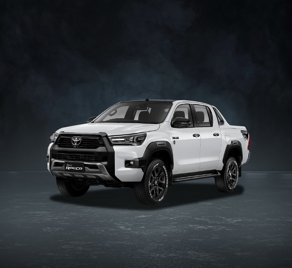White Toyota Hilux Rocco double-cab pickup with black grille and off-road wheels on a dark studio background.